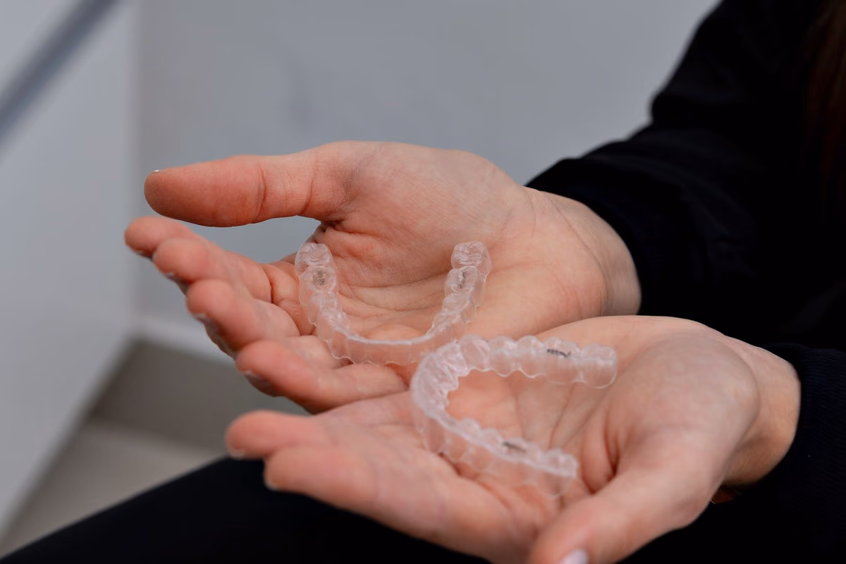 Clear Invisalign aligner trays held in a gloved hand at a dental clinic, illustrating what patients receive across a full Invisalign course in Kuala Lumpur.