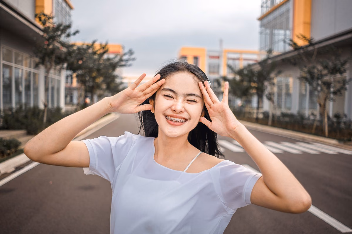 A young woman smiling openly while wearing fixed orthodontic braces, one of the two main teeth-straightening routes in Malaysia.